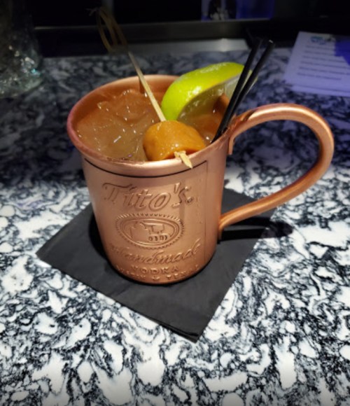 A copper mug filled with a cocktail, garnished with lime and cherries, on a black napkin against a marble surface.