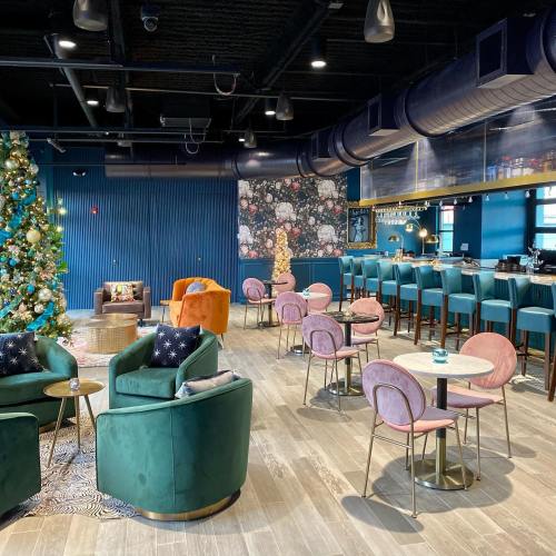 A stylish café interior with green chairs, pink tables, a Christmas tree, and floral wallpaper. Cozy and modern atmosphere.