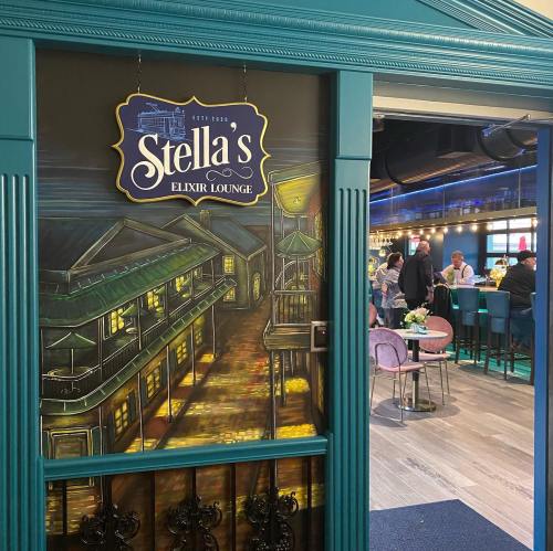 Entrance to Stella's Elixir Lounge, featuring a colorful mural and a lively bar scene in the background.