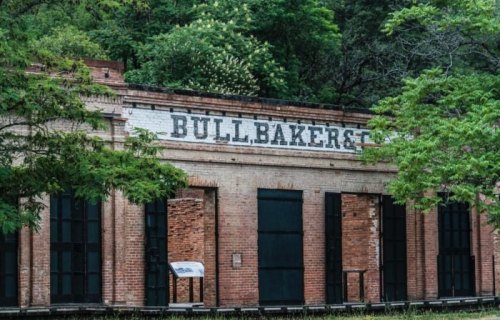 Historic brick building with "BULL BAKER & CO." sign, surrounded by greenery and trees.