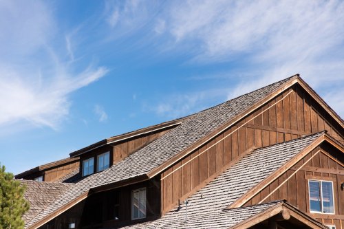 A wooden house with a sloped roof under a clear blue sky and wispy clouds.