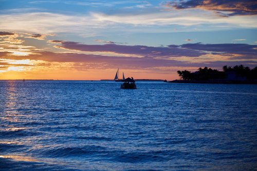 A serene sunset over the ocean with sailboats in the distance and vibrant colors in the sky.