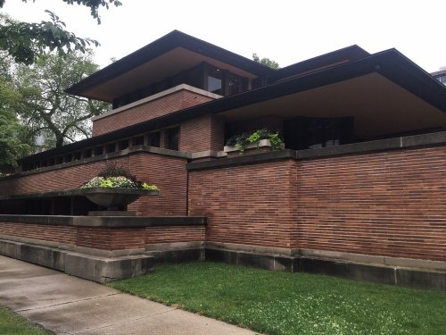 A modern brick building with a flat roof, large windows, and landscaped planters, surrounded by green grass.