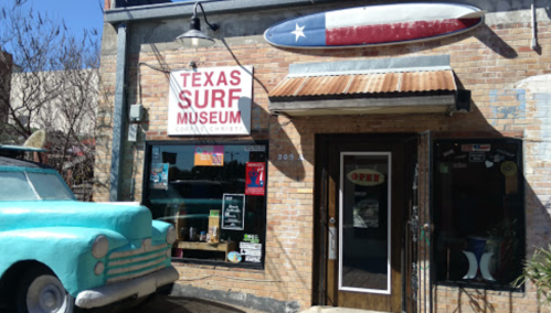 Exterior of the Texas Surf Museum featuring a turquoise vintage car and a surfboard sign above the entrance.