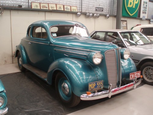 A vintage teal coupe car displayed in a museum, featuring classic design elements and chrome accents.