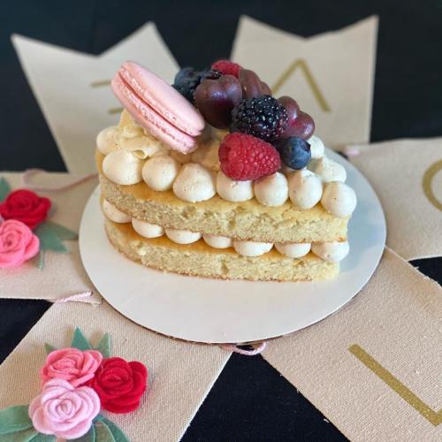 A layered cake topped with fresh berries, a macaron, and decorative flowers on a patterned background.