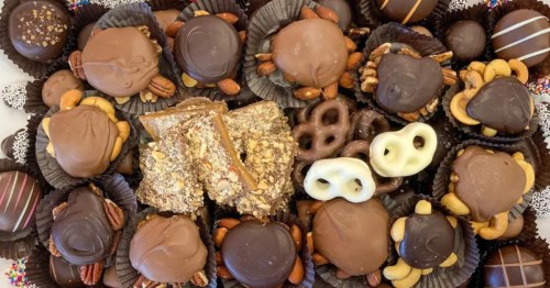 A large, white oval plate with a variety of chocolates like turtles, truffles, and imperials.