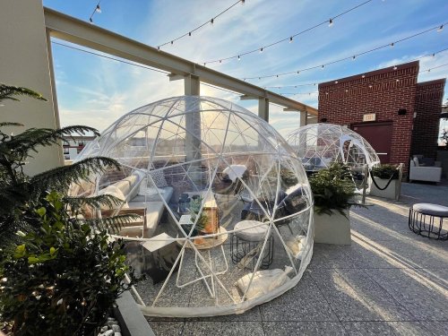 Rooftop terrace with clear geodesic domes, cozy seating, and string lights against a blue sky.