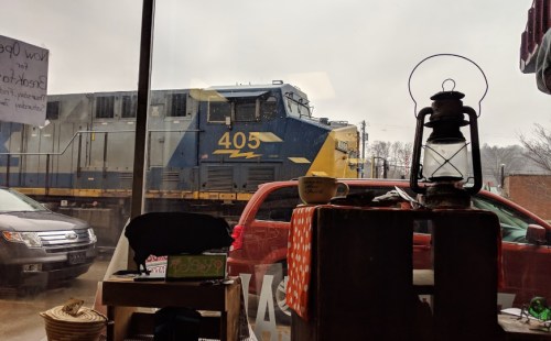 A train passes by outside a shop window, with a vintage lantern and a red vehicle in the foreground.