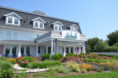 A charming white hotel with a sign reading "The Breaks," surrounded by colorful flowers and greenery on a sunny day.