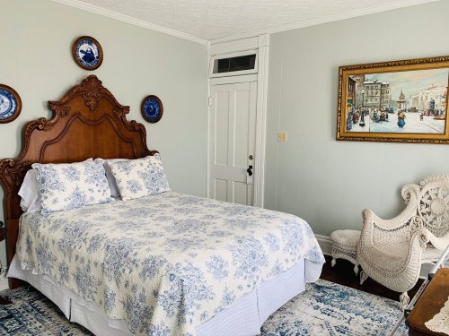 Cozy bedroom featuring a wooden bed, blue and white bedding, decorative plates, and a vintage painting.