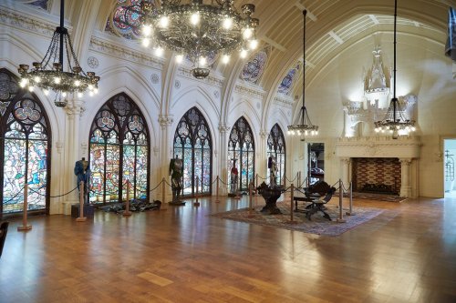 Interior of a grand hall featuring stained glass windows, chandeliers, and ornate architectural details.
