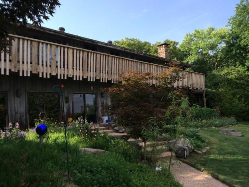 A rustic house with wooden balconies, surrounded by lush greenery and a stone pathway leading to the entrance.