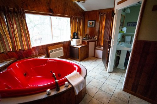 A cozy bathroom featuring a red jacuzzi tub, wooden walls, and a window with natural light.