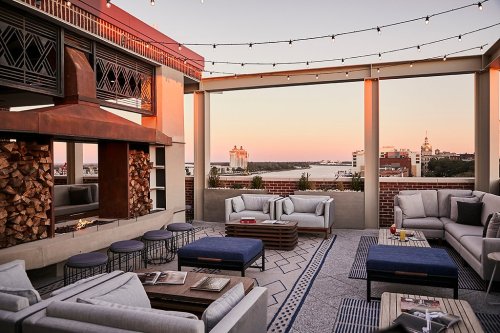 Rooftop lounge with cozy seating, a fireplace, and city skyline views at sunset, adorned with string lights.