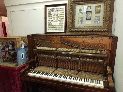 An antique piano with exposed mechanics, surrounded by framed photographs and a decorative display.