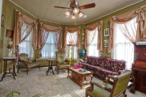 Cozy vintage living room with floral curtains, a patterned sofa, wooden furniture, and warm lighting.