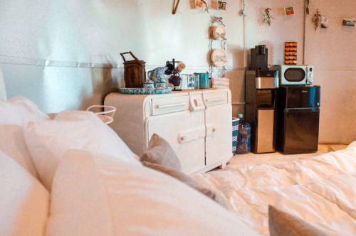 Cozy interior of a room with a bed, vintage furniture, and a small kitchen area featuring a microwave and fridge.
