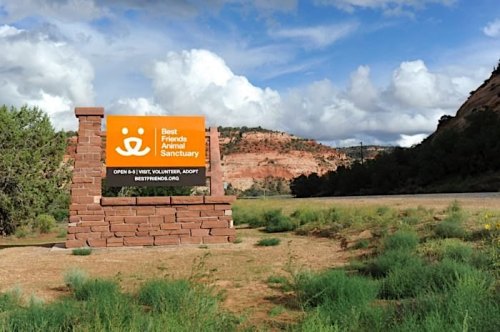 Sign for Best Friends Animal Sanctuary with mountains and clouds in the background, promoting adoption and volunteering.