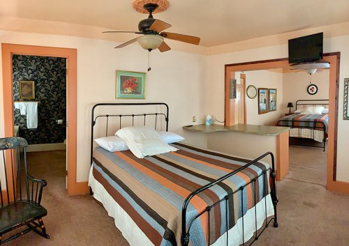 Cozy bedroom with a striped bedspread, ceiling fan, and adjoining room featuring another bed and a TV.