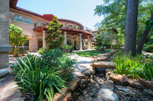 A lush garden with a stone pathway, leading to a spacious, elegant home surrounded by greenery and trees.