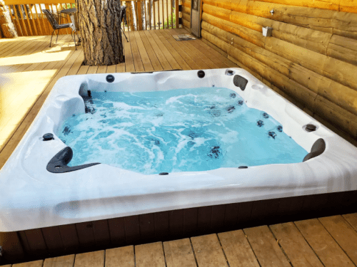 A hot tub filled with water, situated on a wooden deck next to a log cabin.