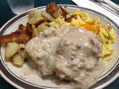 A plate of breakfast featuring biscuits smothered in gravy, scrambled eggs, and crispy potatoes.