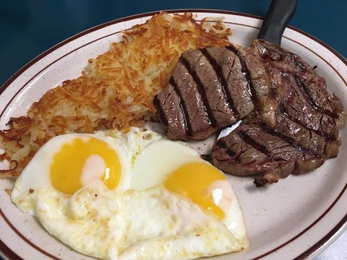 A plate with two fried eggs, a portion of hash browns, and a grilled steak, served on a white dish with a brown rim.