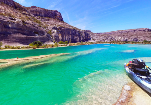 A serene turquoise river with rocky cliffs and a kayak on the shore under a clear blue sky.