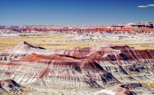 Vast, colorful badlands with layered red and gray hills under a clear blue sky.