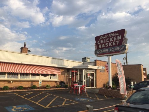 Exterior of Del Rhea Chicken Basket, a casual restaurant with a sign, outdoor seating, and a cloudy sky.