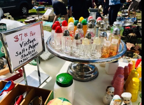 A display of vintage salt and pepper shakers in various colors on a silver tray, with a sign priced at $7.00 per pair.