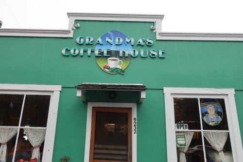 A green coffee house with a sign reading "Grandma's Coffee House" and a cup graphic, featuring large windows.