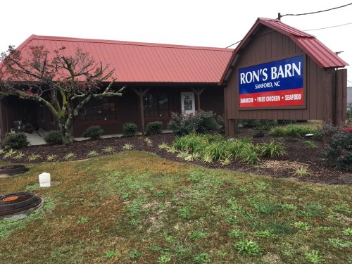 Exterior of Ron's Barn restaurant in Sanford, NC, featuring a red roof and a sign advertising barbecue, fried chicken, and seafood.