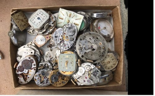 A box filled with various vintage watch movements and parts, showcasing intricate gears and designs.