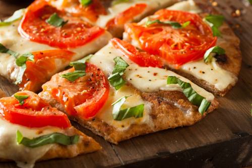 Freshly baked flatbread pizza topped with melted cheese, sliced tomatoes, and fresh basil on a wooden board.