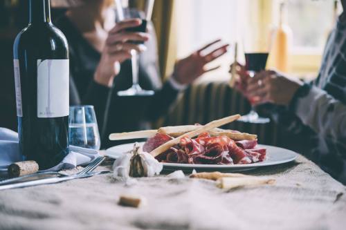 A table set with wine glasses and a plate of cured meats, with two people enjoying drinks in the background.