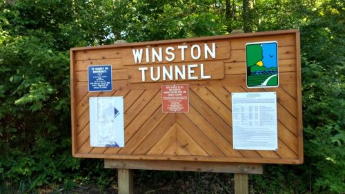 Wooden sign for Winston Tunnel, featuring informational plaques and surrounded by greenery.