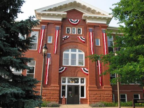 Historic brick building adorned with American flags and bunting, surrounded by greenery.