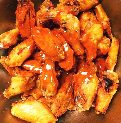 A bowl filled with crispy chicken wings coated in a spicy orange sauce.