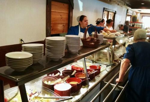 A buffet with various dishes and bowls, with staff serving food in a casual dining setting.