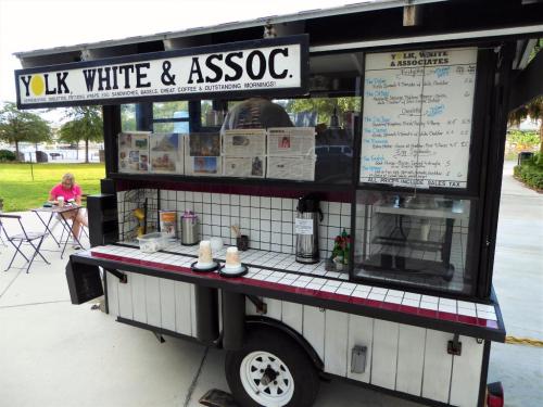 A food truck named "Yolk White & Assoc." with a menu board, serving breakfast items and coffee in a park setting.