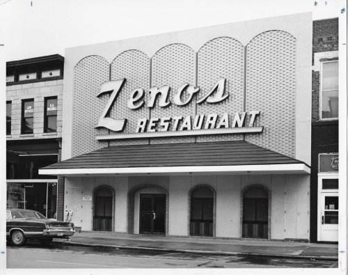 Black and white photo of Zeno's Restaurant exterior, featuring a large sign and a classic car parked in front.