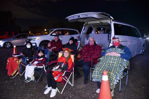 A group of people sitting in chairs by a van at night, wrapped in blankets, enjoying an outdoor event.