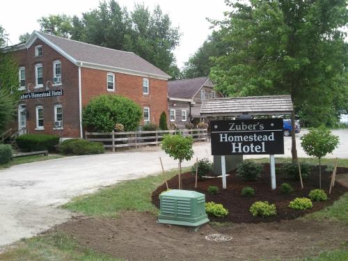 A brick building with a sign reading "Zuber's Homestead Hotel," surrounded by greenery and a gravel path.