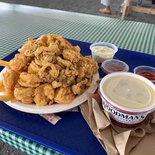 A plate of fried seafood, including shrimp and fish, served with dipping sauces on a checkered tablecloth.