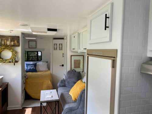 Cozy interior of a camper with a bed, sofa, and kitchenette, featuring warm decor and natural light.