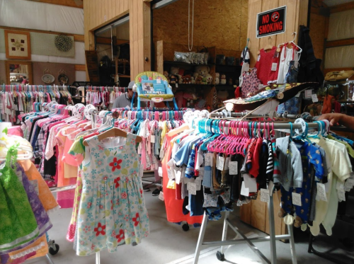 A colorful display of children's clothing on racks in a shop, with a "No Smoking" sign visible in the background.