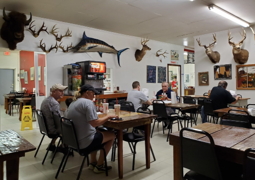 A casual dining area with wooden tables, patrons eating, and taxidermy decor on the walls.
