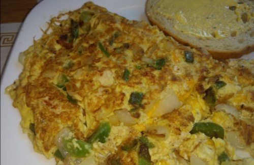 A fluffy omelette with green peppers and onions, served with a slice of buttered bread on the side.